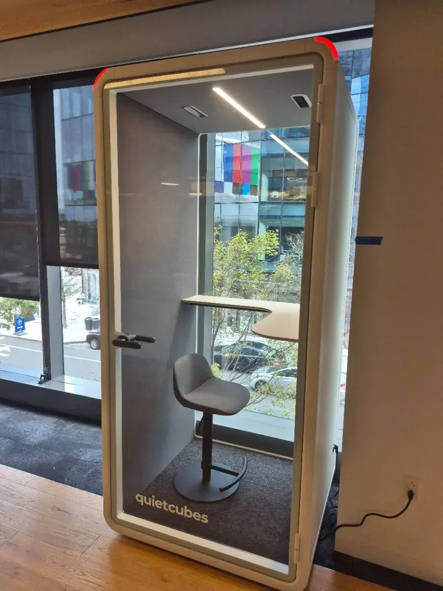 Contact Us Compact office phone booth with padded stool and curved desk by window for private work spaces