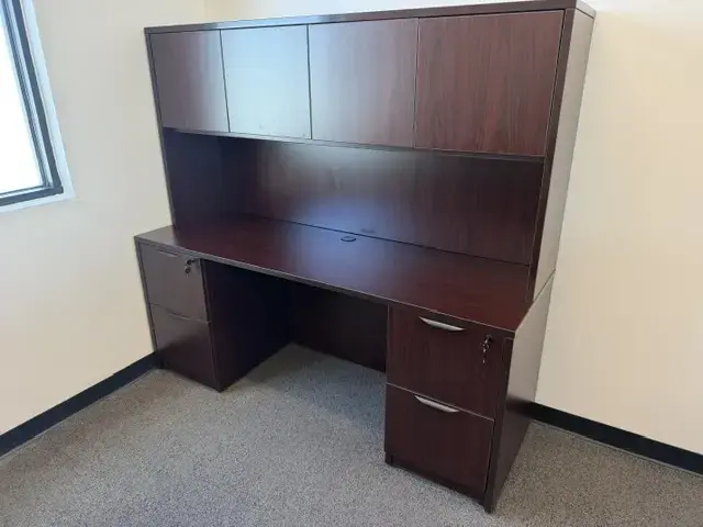 Contact Us Dark wood office desk with hutch and multiple drawers in a bright carpeted office room