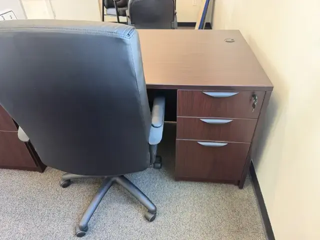 Contact Us Office workspace with dark brown wooden desk and black swivel chair on carpeted floor