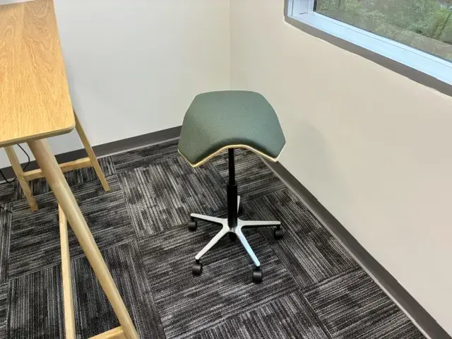 Creating a Finished Workplace in Miami Ergonomic saddle stool with wheels next to wooden desk in office corner with large window