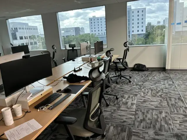 Creating a Finished Workplace in Miami Modern office workspace with several ergonomic chairs and computer monitors near large windows overlooking city buildings