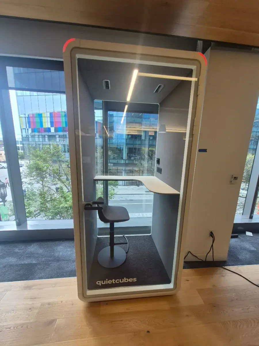 Contact Us Modern single-person soundproof work pod with stool and desk near large office windows