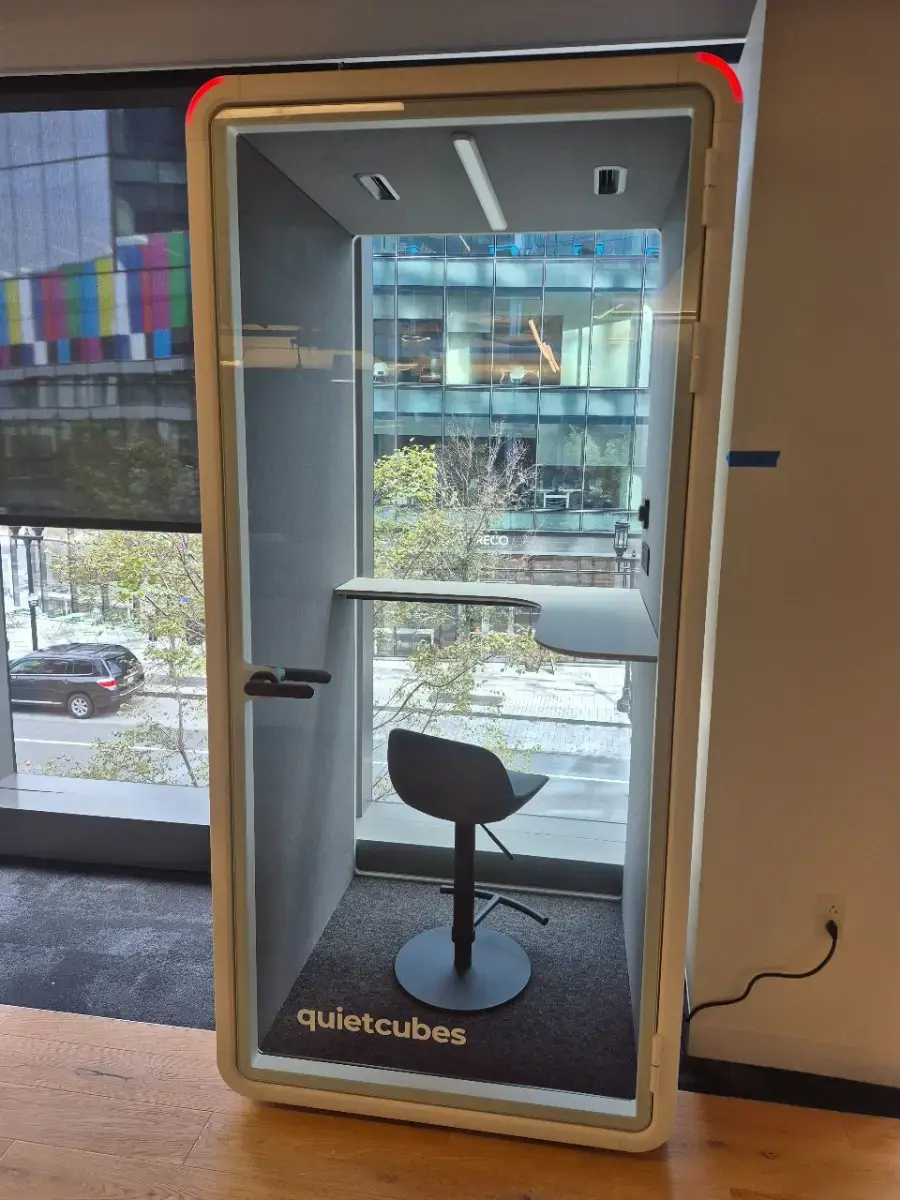 Contact Us Small quiet work booth featuring a high stool and built-in desk by window for focus work