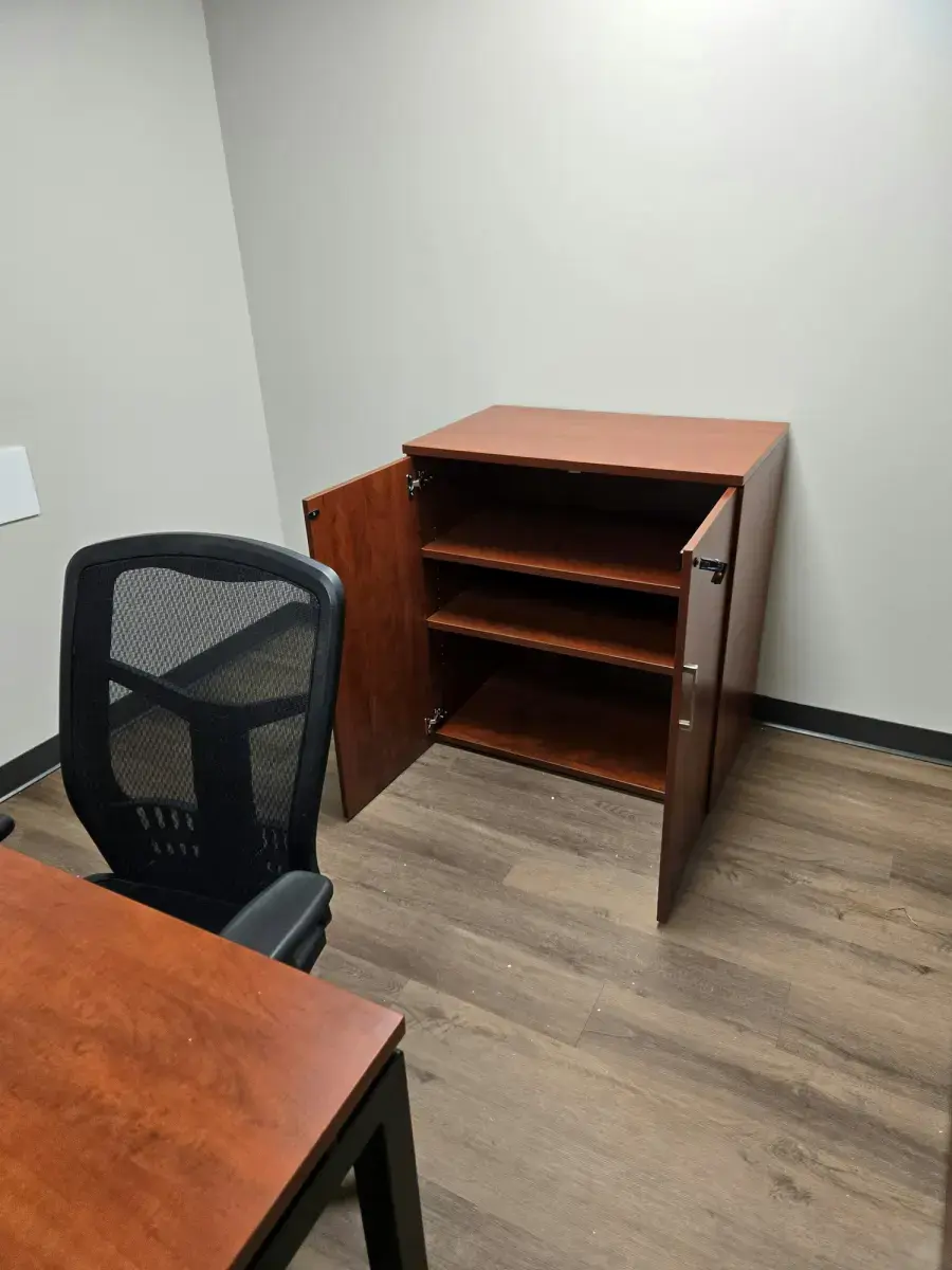 Let Us Help Build Your Next Workspace Open wooden storage cabinet with empty shelves beside a desk and mesh chair in a small office